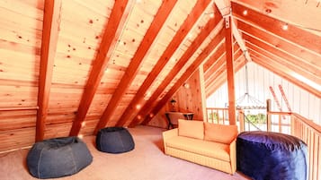 An attic room with a wooden ceiling, a sofa, two bean bags, and a dining table.