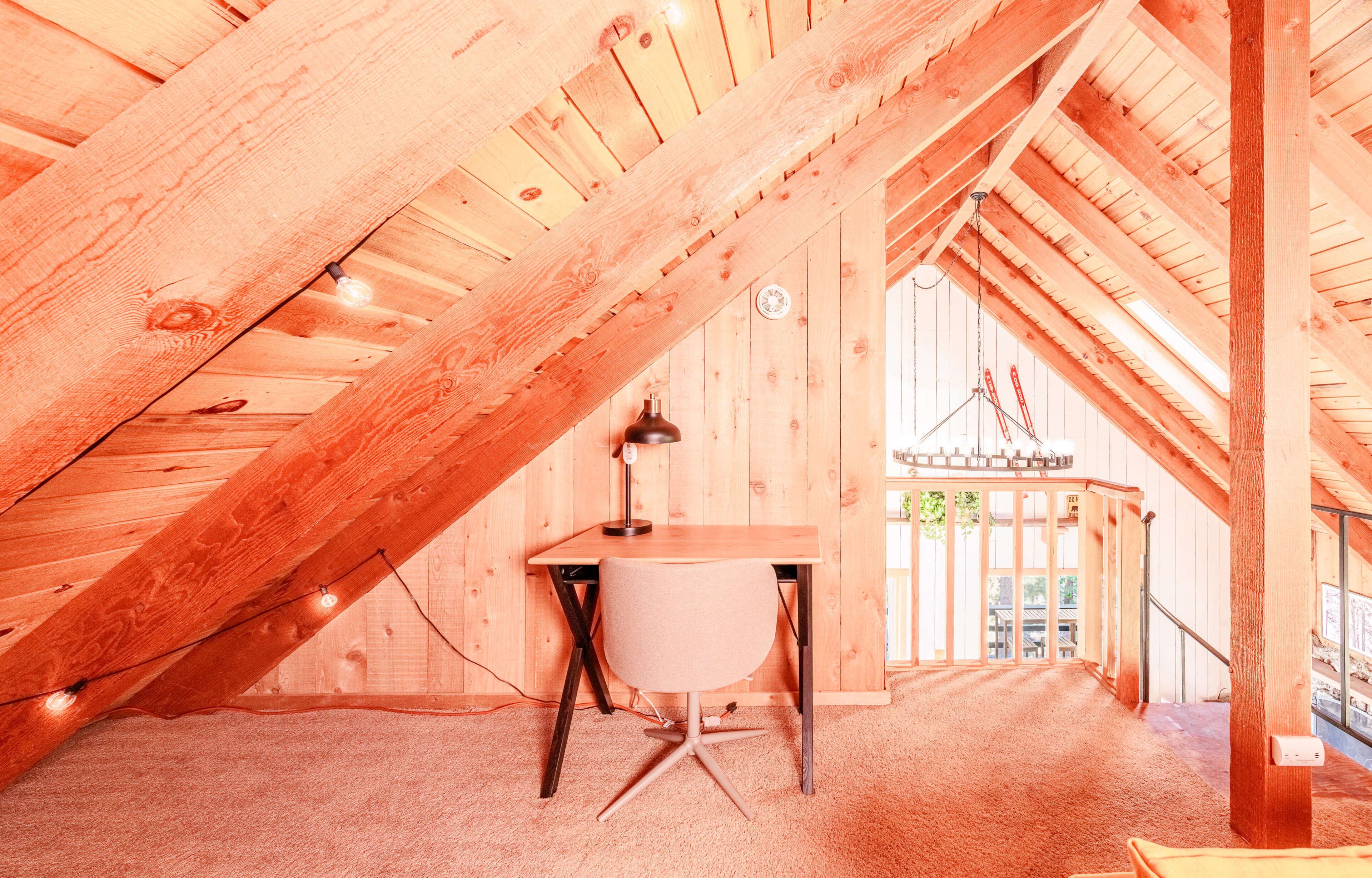 Une chambre mansardée avec un bureau, une chaise et un luminaire suspendu.