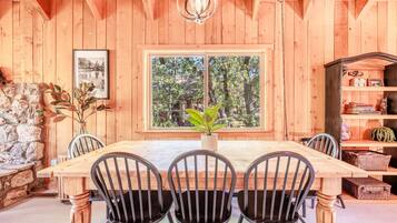 Comedor de madera con ventana grande, una araña y pared de piedra.