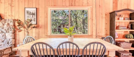 A wooden dining room with a large window, a chandelier, and a stone wall.