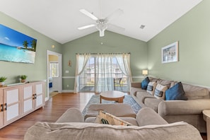 A spacious living room with a ceiling fan, a large window with curtains, a sofa set, and a wooden cabinet. - Magnolia North 4834-304 (Myrtle Beach)