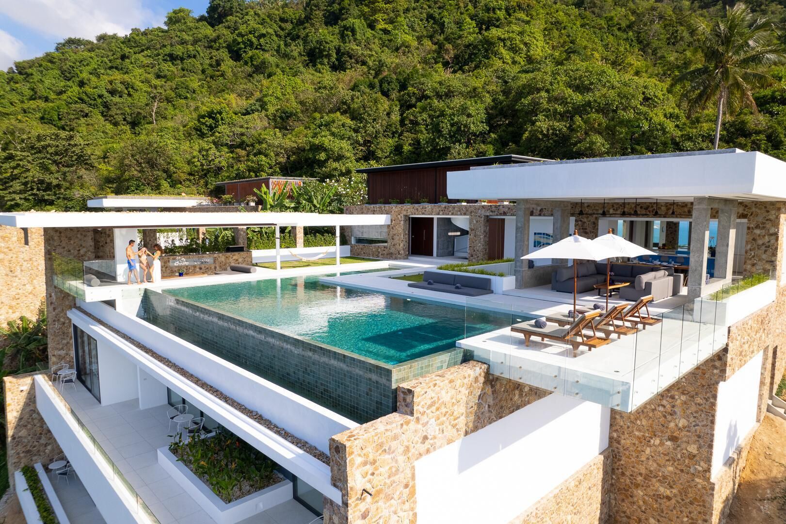 A modern house with a large swimming pool, outdoor seating, and a view of a forested hill.
