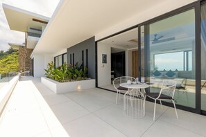 Un patio moderno al aire libre con barandilla de vidrio, mobiliario blanco y vista al mar.