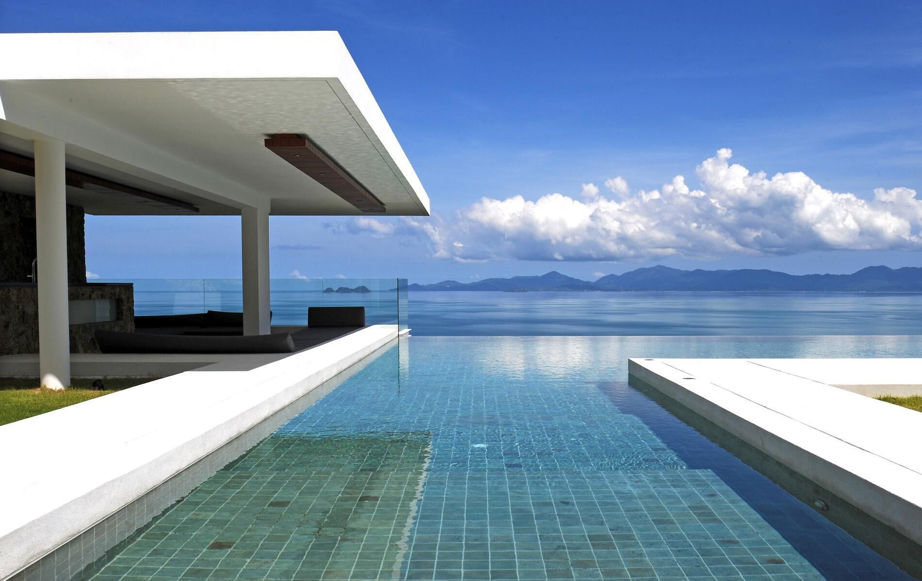 Une piscine à débordement moderne offrant une vue dégagée sur l’océan et les montagnes en arrière-plan.