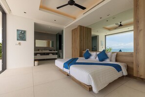 Un dormitorio moderno con una cama grande, cabecera de madera, ventilador de techo y vista al mar.