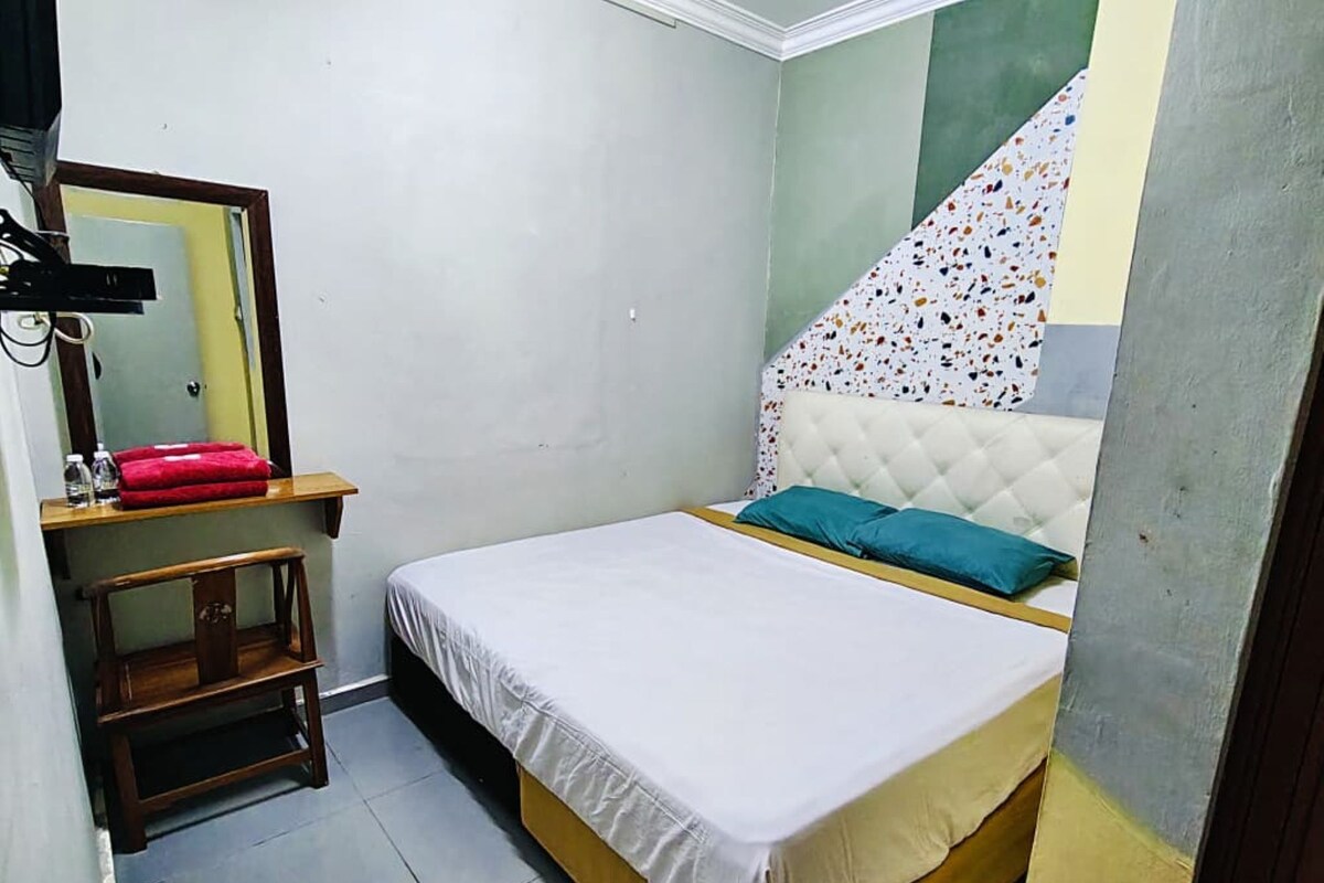 Ein Schlafzimmer mit einem Bett, einem Spiegel, einem kleinen Holzschemel und einer Wand mit einem farbenfrohen Muster.