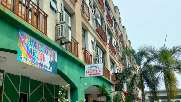 Un hotel con fachada verde, varios balcones y plantas en macetas en la zona de entrada.
