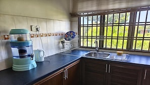 Una cocina con dispensador de agua, tetera, escurreplatos y ventana con vistas a zonas verdes.