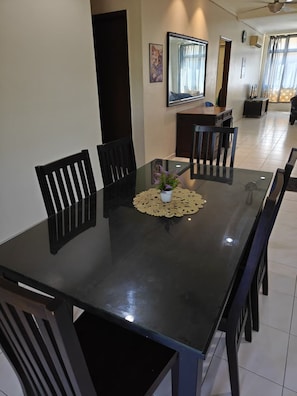 Uma sala de jantar com uma mesa retangular, cadeiras pretas, uma pequena planta em vaso e um jogo americano decorativo.