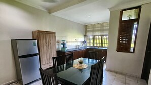 Una cocina compacta con refrigerador, armarios de madera, una mesa de comedor con sillas y un ventanal con persianas.
