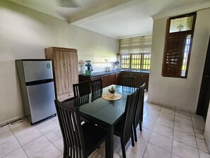 Eine kompakte Küche mit Kühlschrank, Holzschränken, einem Esstisch mit Stühlen und einem Fenster mit Jalousien.