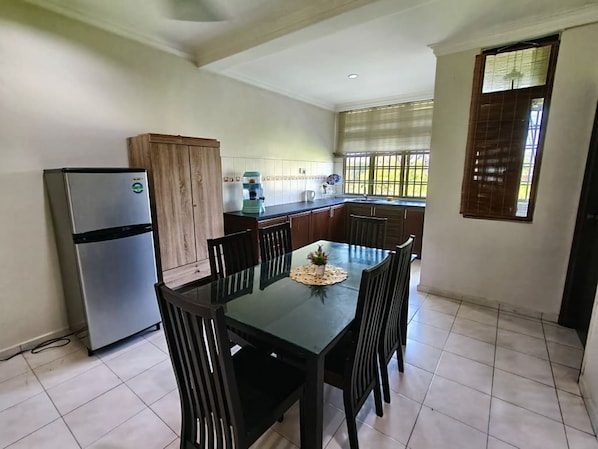 Una cocina compacta con refrigerador, armarios de madera, una mesa de comedor con sillas y un ventanal con persianas.