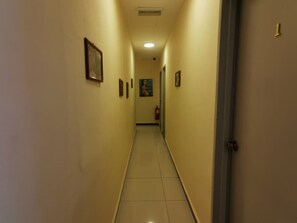 Un pasillo estrecho con piso de baldosas, una puerta a la derecha y varias fotografías enmarcadas en las paredes.