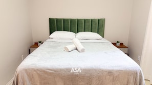 A neatly made bed with a green headboard, two white pillows, and a rolled white towel. There are two small bedside tables with potted plants. - ASA Verona Park 06 2 Bedrooms Single Story House Timbo (Timbo)