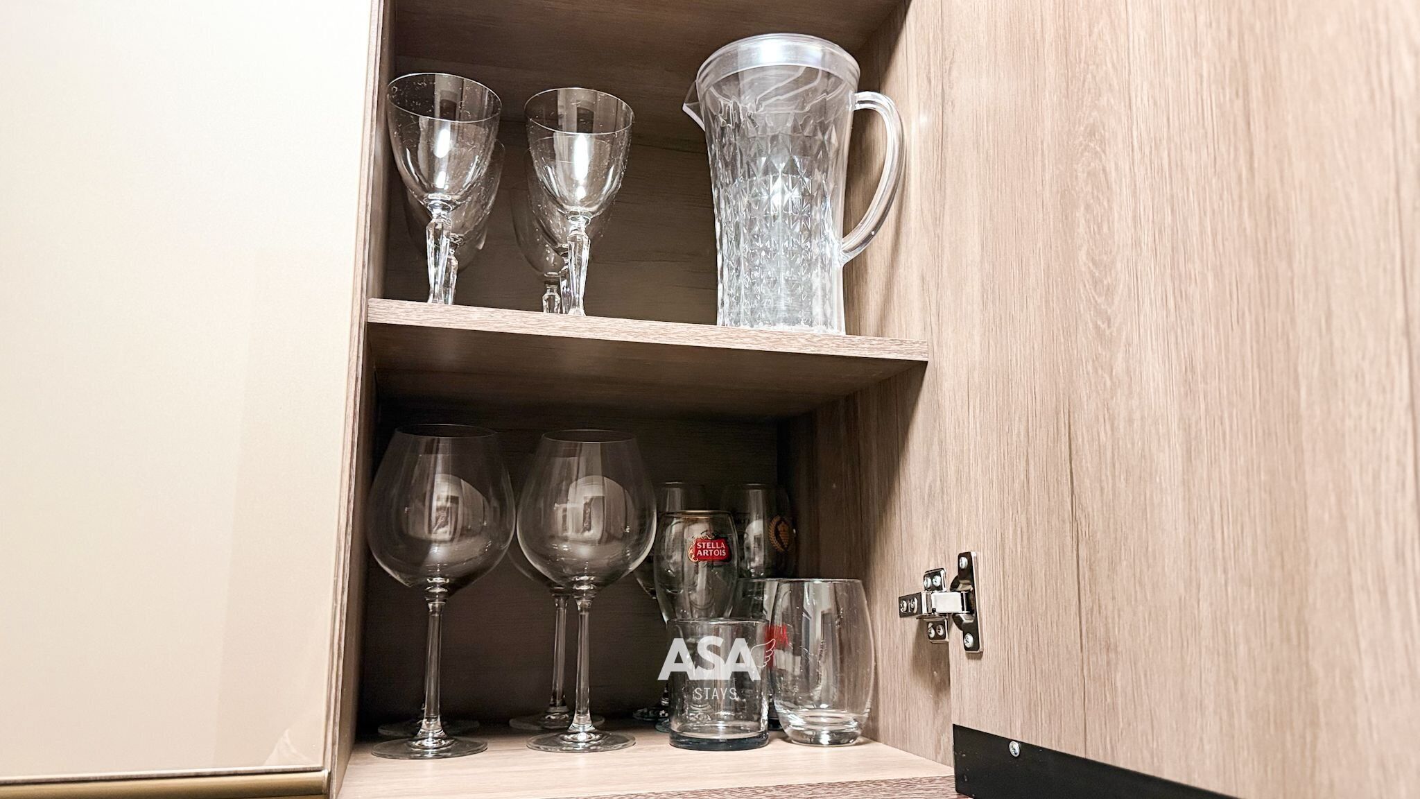 A wooden cabinet with shelves holding various glassware, including wine glasses and a pitcher.