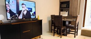 A dining area with a television displaying a concert, a wooden dining table, and chairs.