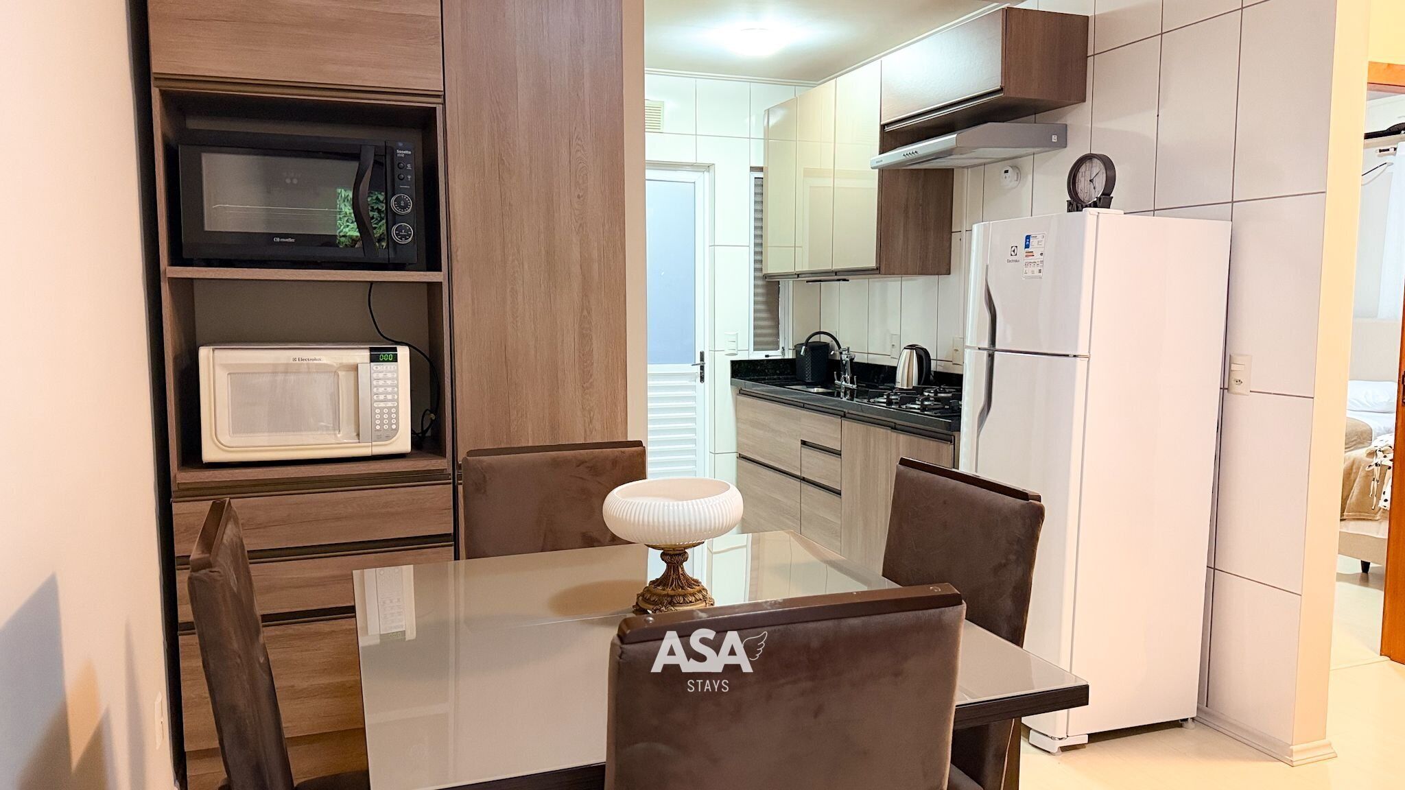 Una cocina compacta equipada con microondas, estufa y refrigerador. Hay una mesa de comedor con sillas y una lámpara decorativa.
