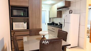 Una cocina compacta equipada con microondas, estufa y refrigerador. Hay una mesa de comedor con sillas y una lámpara decorativa.