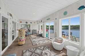 A covered outdoor area with a view of a lake, furnished with wicker chairs and a wooden table. - GREENVILLE GETAWAY:  (Greenville, MI) Lakefront on Perch Lake, Sleeps 6-Kayak, Paddle Boat-Dock! (Greenville)