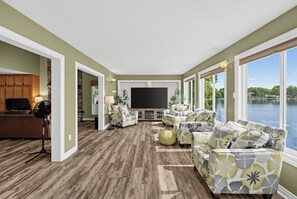 A spacious living room with a large flat-screen TV, comfortable seating, and a view of a body of water. - GREENVILLE GETAWAY:  (Greenville, MI) Lakefront on Perch Lake, Sleeps 6-Kayak, Paddle Boat-Dock! (Greenville)