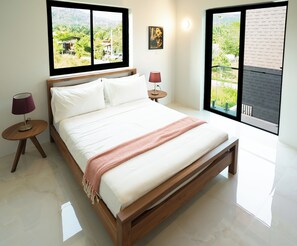 Een moderne slaapkamer met een houten bed, wit beddengoed, een rode plaid, twee nachtlampjes en grote ramen met uitzicht op groen en een gebouw.