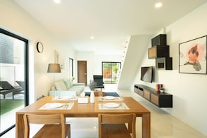 A modern dining area with a wooden table set for four, a sofa in the background, and a TV mounted on the wall.