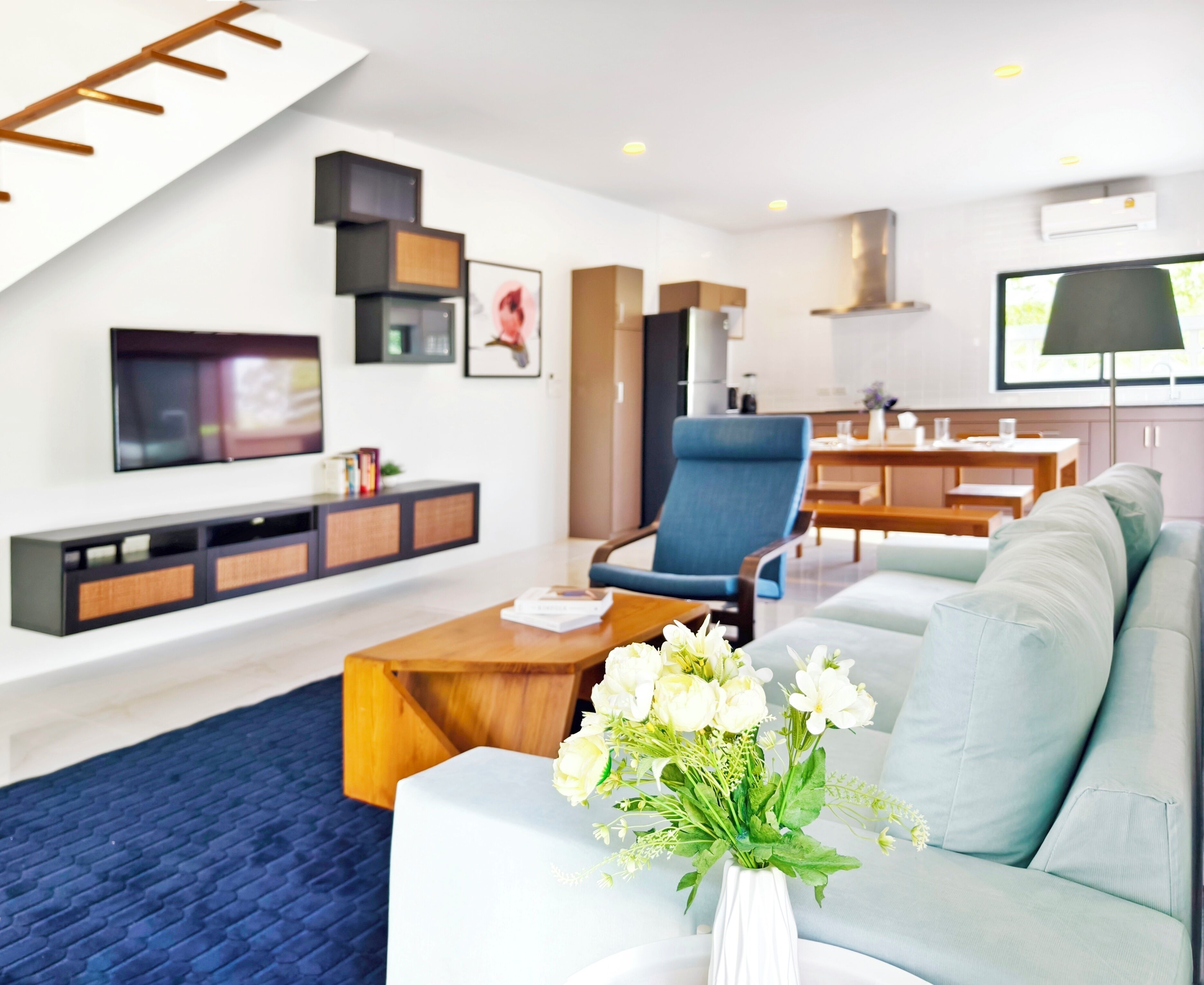 Ein modernes Wohnzimmer mit Sofa, Couchtisch und Fernseher. Im Hintergrund befindet sich ein Essbereich mit Tisch und Stühlen.