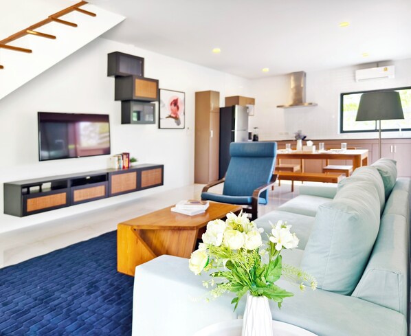 A modern living room with a sofa, coffee table, and a TV. There is a dining area with a table and chairs in the background.