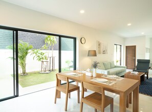 Un salon moderne comprenant un coin repas, de grandes portes-fenêtres coulissantes donnant sur un jardin, un canapé, une table basse et une lampe.