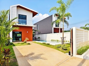 Een modern huis met twee verdiepingen, een zwembad, een overdekt terras en een verzorgde tuin.