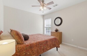 Quarto com cama, ventoinha no teto, cômoda, espelho e janela com persianas.