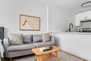 A modern living room with a grey sofa, a wooden coffee table, and a kitchen area with white cabinets and a black faucet. - Blueground | Denny Triangle, gym, nr Pike Place (Seattle)
