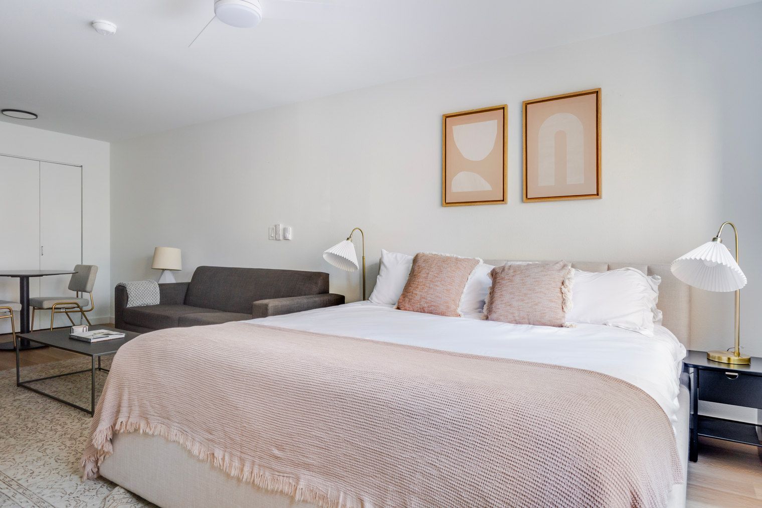 A hotel room with a large bed, a sofa, a desk, and a chair. There are two wall-mounted lamps and a ceiling light.