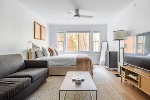 Ein modernes Wohnzimmer mit Sofa, einem Bett mit Blick, einem Fernseher und einem Deckenventilator.