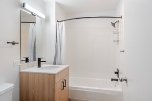 Un baño moderno con una bañera blanca, un mueble de tocador de madera, un espejo y una cortina de ducha.
