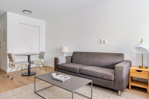Una sala de estar moderna con un sofá gris, una mesa redonda de centro, una mesita auxiliar y una lámpara.