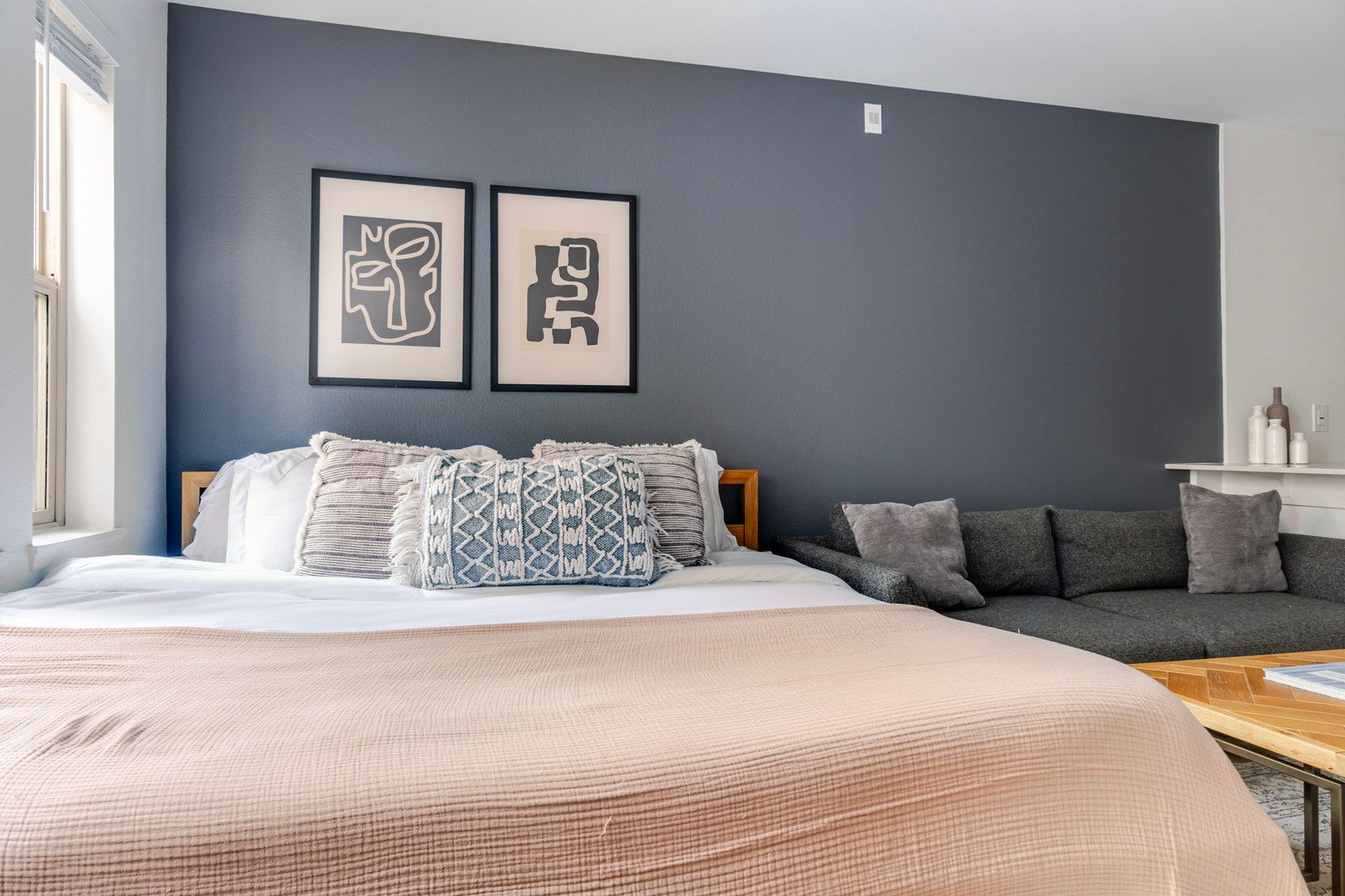 A bedroom with a large bed, a grey sofa, and two framed abstract artworks on the wall.