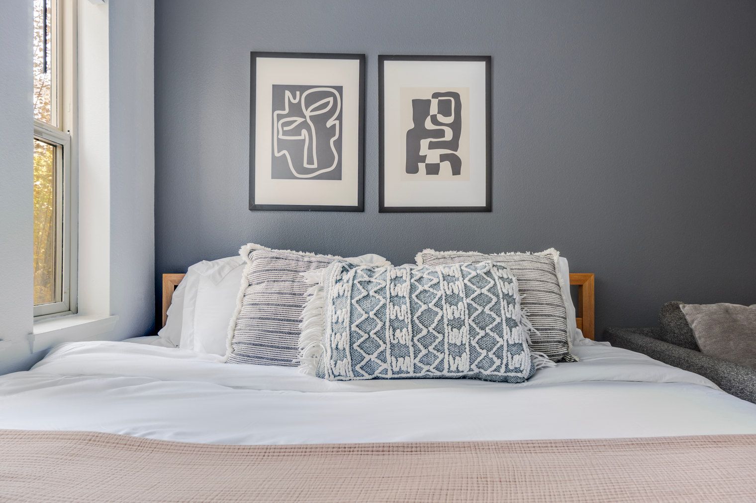 A bedroom with a bed, two framed artworks, and a window.