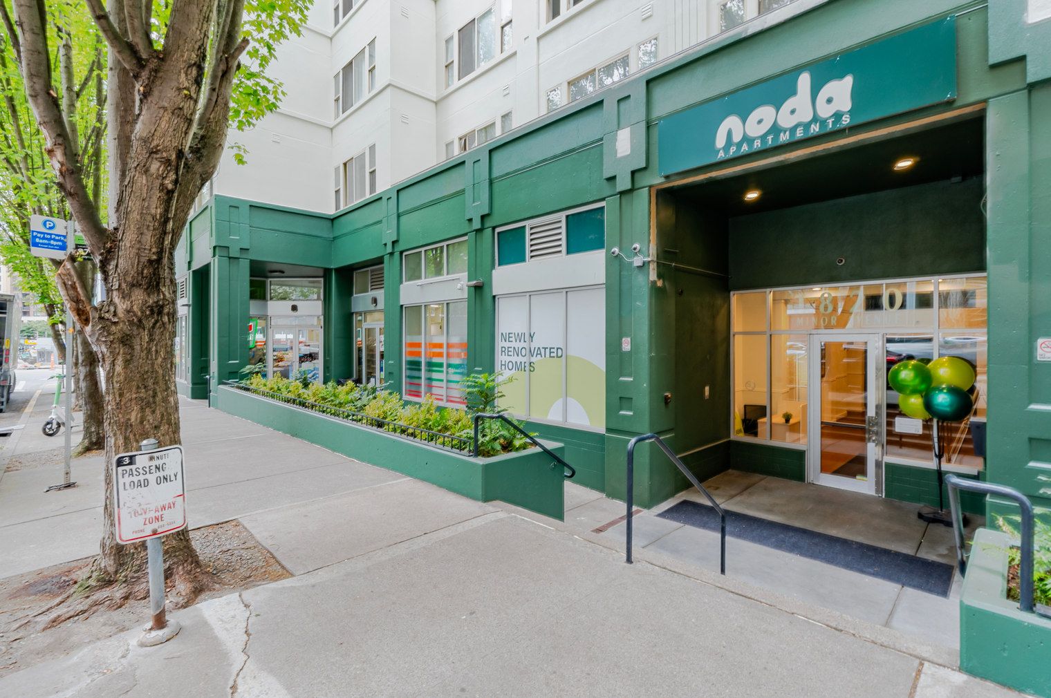 A building with a green facade, a sign for 'noda apartments,' and a 'newly renovated homes' advertisement.