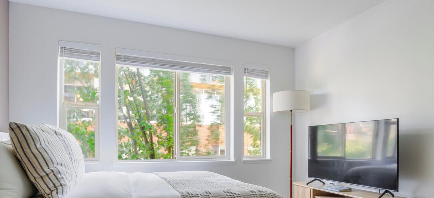 Quarto com cama, televisão e janela com persianas.