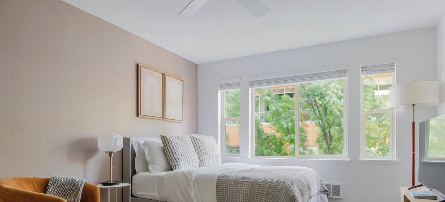 Un dormitorio con cama, mesitas de noche, lámpara y ventanas con vistas a zonas verdes.