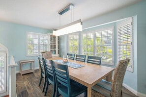 A dining area with a wooden table, six chairs, and a hanging light fixture. - Surrounded by Sea Breezes (Anna Maria)