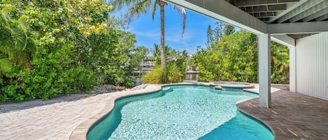 A swimming pool with a curved design, surrounded by lush greenery and a covered patio area.