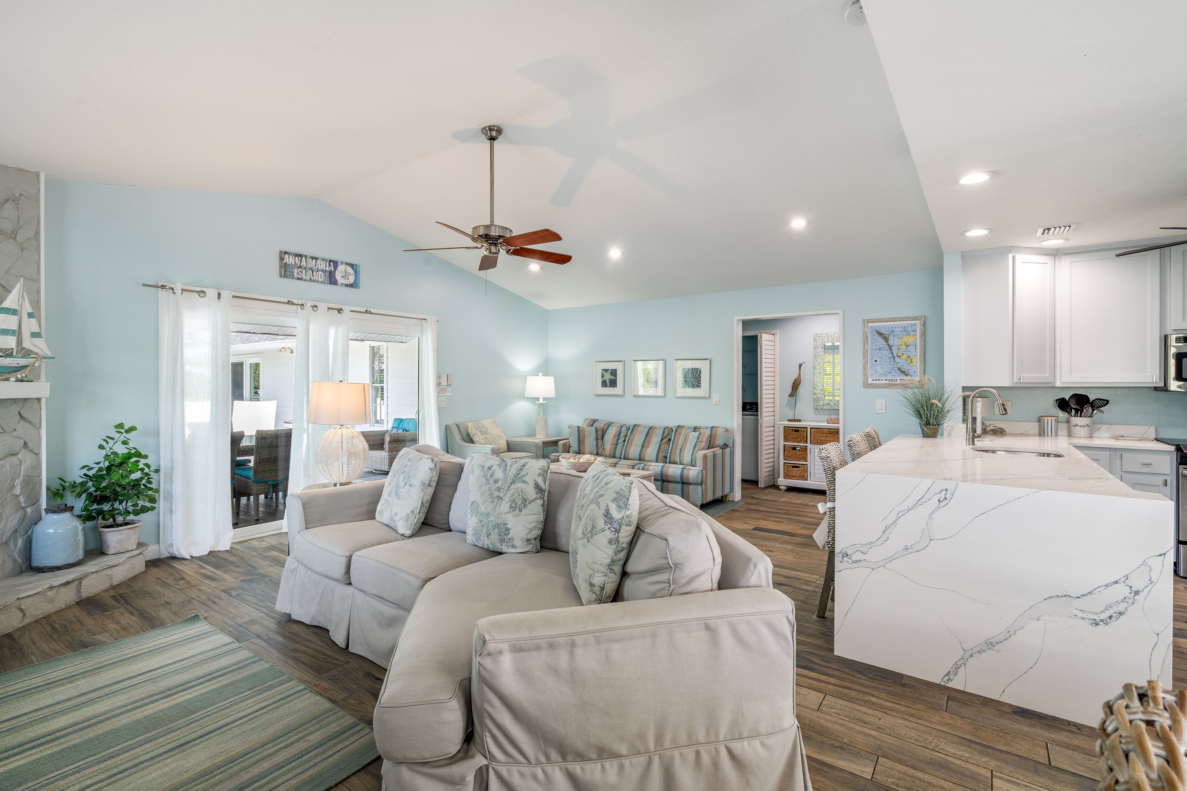 A spacious living area with a sofa, a ceiling fan, and a kitchen with a marble countertop.