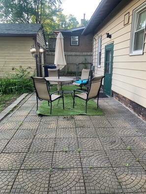 Een terras met een tafel en stoelen, een groene deur en een hek.