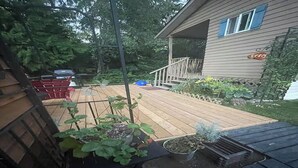 A wooden deck with potted plants, a red chair, and a house with a porch. - Suite Amour Hobby Farm Bed & Breakfast (Qualicum Beach)