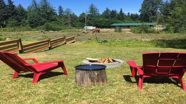 A fenced outdoor area with red chairs, a fire pit, and a horse in the background. - Suite Amour Hobby Farm Bed & Breakfast (Qualicum Beach)