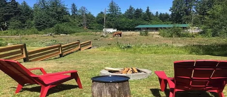 A fenced outdoor area with red chairs, a fire pit, and a horse in the background.