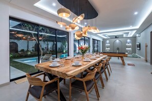 A modern dining area with a long wooden table, multiple chairs, and pendant lighting. - Villa Kaori (Tibubeneng)
