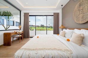 A modern bedroom with a large bed, a desk, and a view of greenery outside. - Villa Kaori (Tibubeneng)